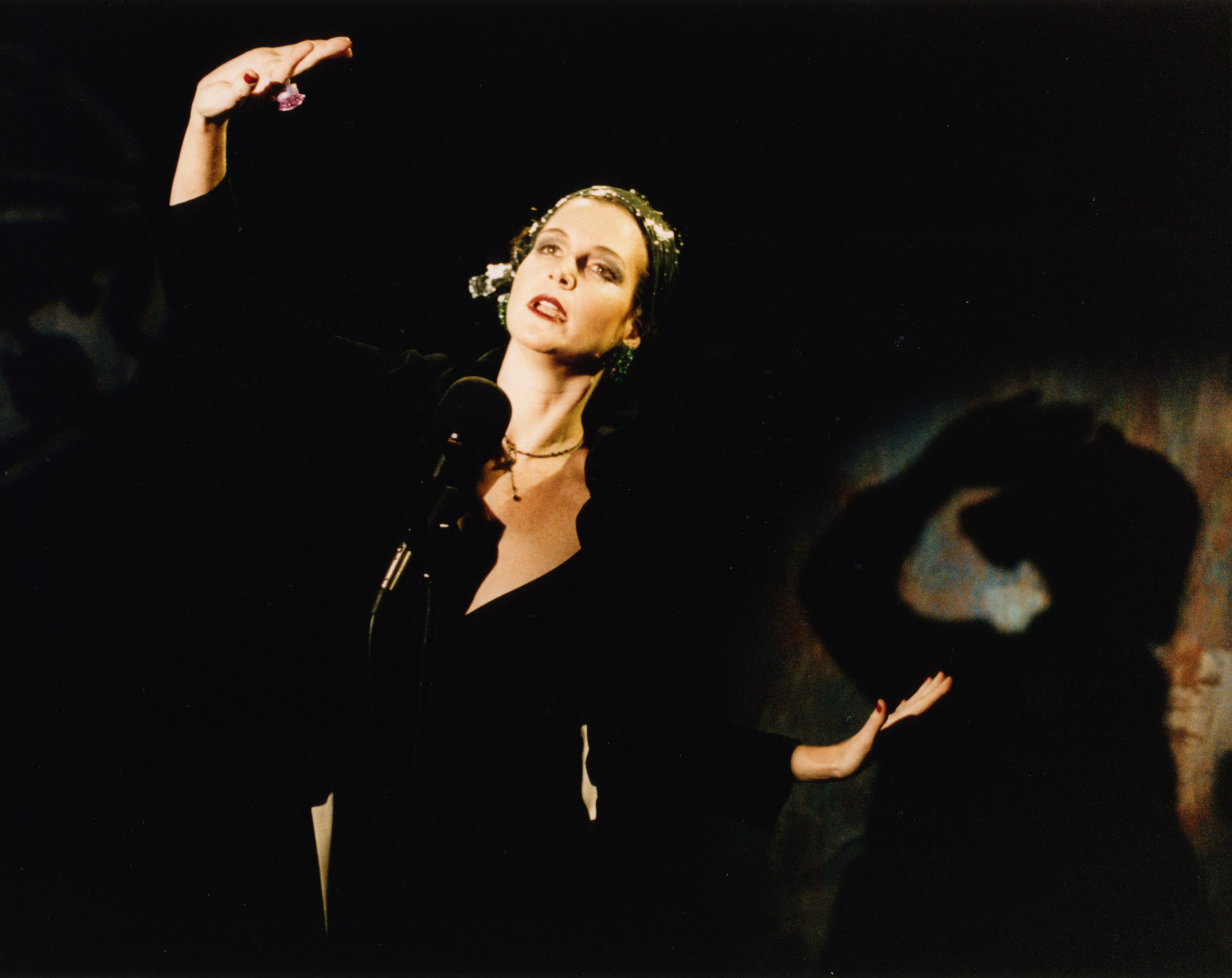 An actress performs a monologue on a dim stage while the audience watches in silhouette — When (1999)